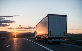 Heavy-duty truck hauling goods on a rural highway at sunrise.