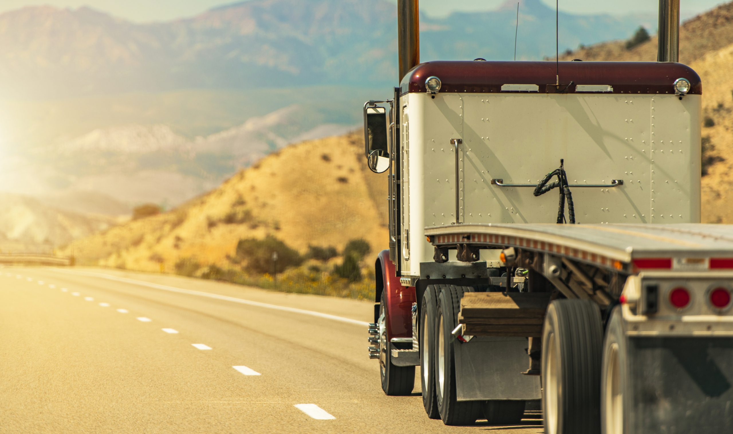 Semi-truck hauling a flatbed trailer through rolling hills.