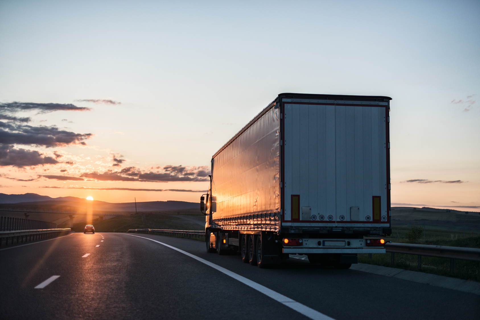 Heavy-duty truck hauling goods on a rural highway at sunrise.