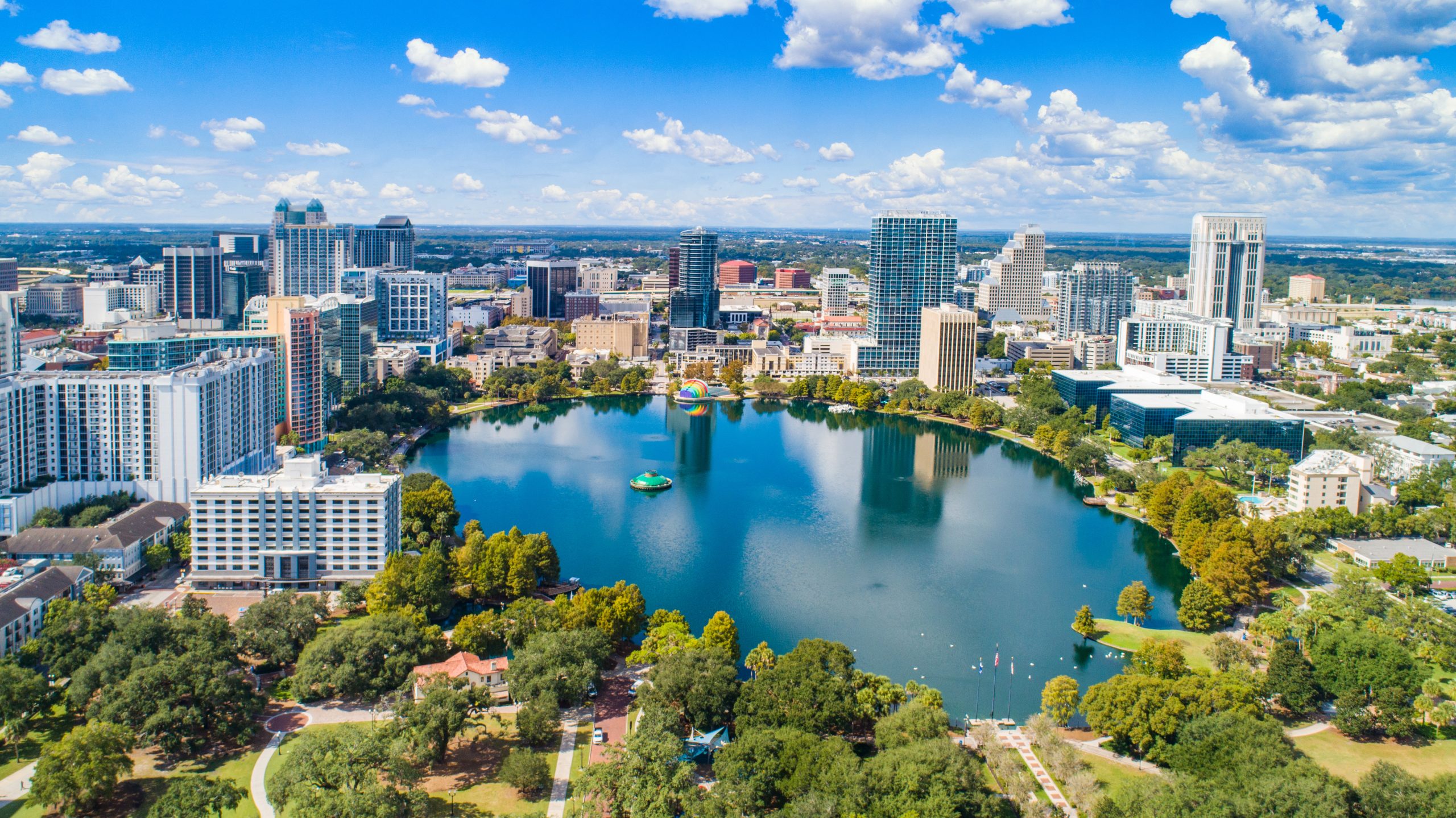 Aerial view of downtown Orlando, Florida, featuring Lake Eola and surrounding high-rise buildings on a sunny day.