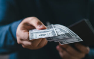 A close-up of a hand passing cash or a check to a truck driver, with a truck visible in the background.