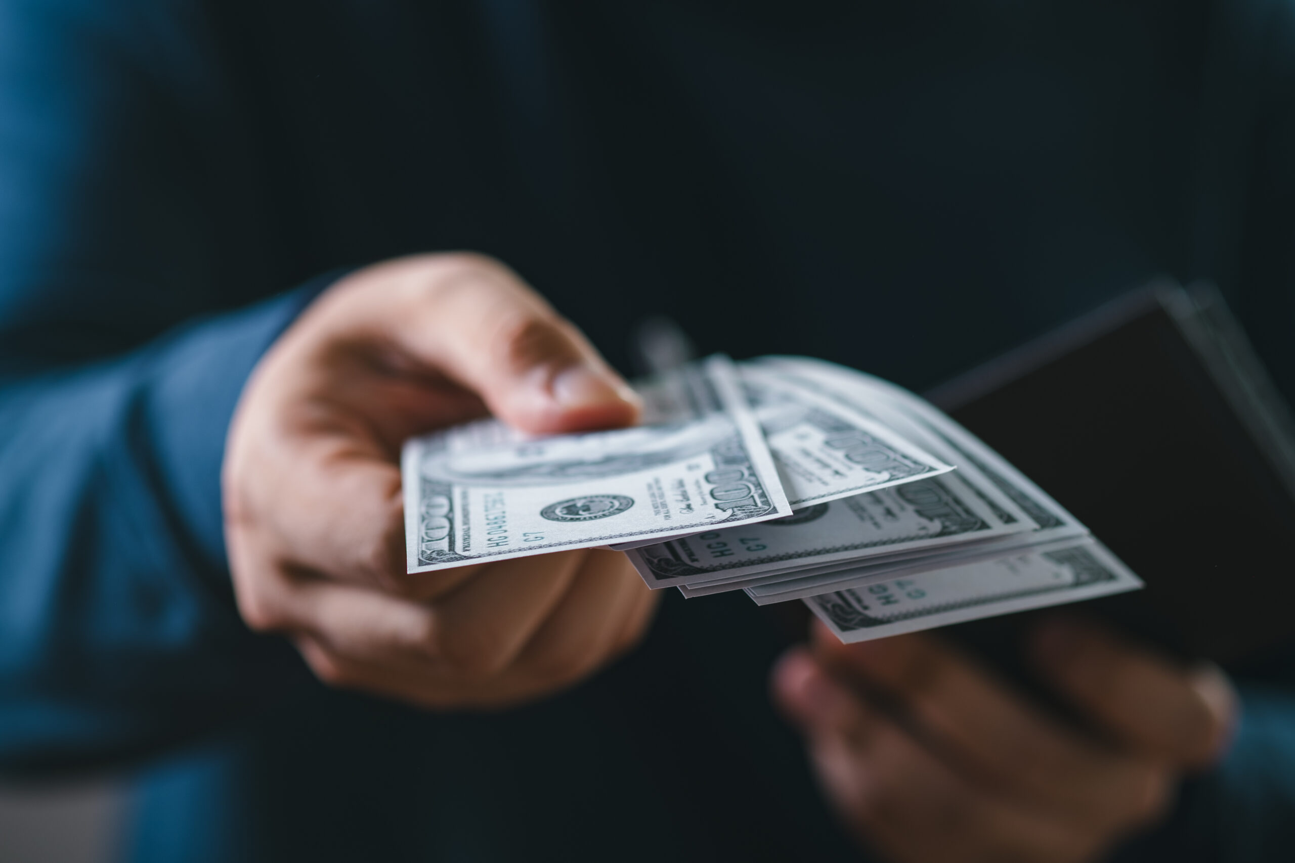 A close-up of a hand passing cash or a check to a truck driver, with a truck visible in the background.